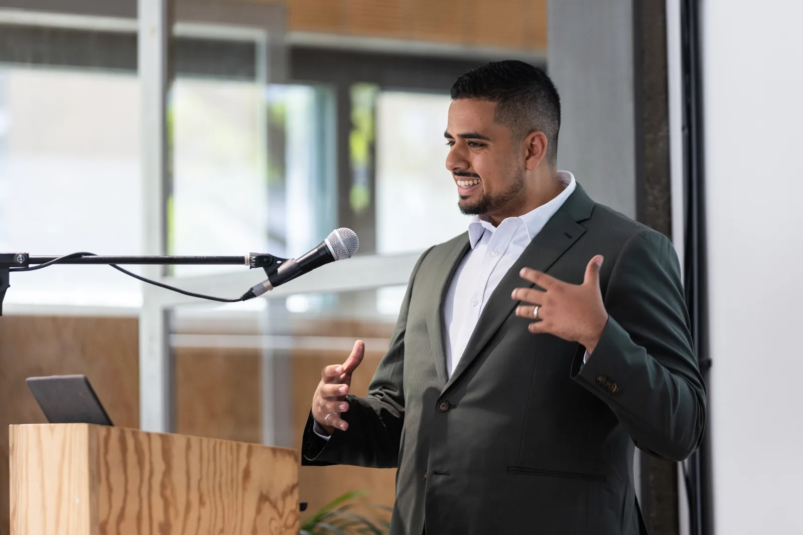 Mark speaking at the mic in an olive suit